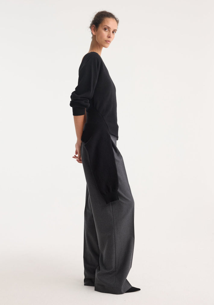 Model wearing Off Shoulder Single Sleeve Top, black, with asymmetric design and draped hemline, paired with high-waisted, wide-leg trousers, showcasing minimalist elegance.