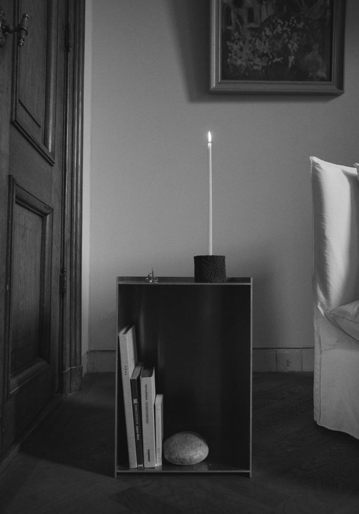 Round Candle Holder crafted from lava stone, holding a lit candle atop a cube side table with books and a stone, set in a serene interior.
