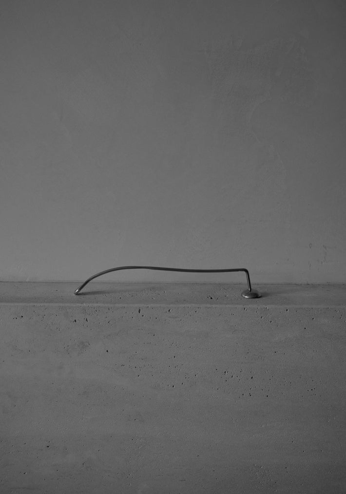 Silver Candle Stopper features an elegantly spiraled stainless steel handle, resting on a concrete slab, blending minimalist design with functional sophistication for extinguishing candles.