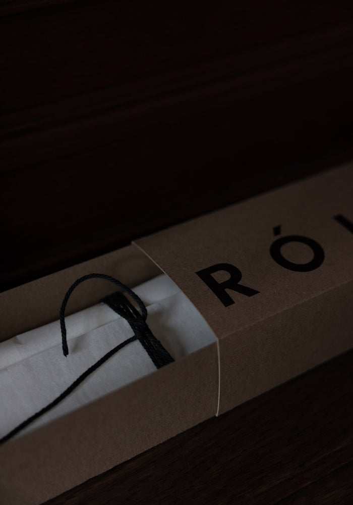 Kraft-paper box revealing a white tissue-wrapped item, likely the Candle Stopper | silver, tied with a black cord, partially showing “RÖ” logo.