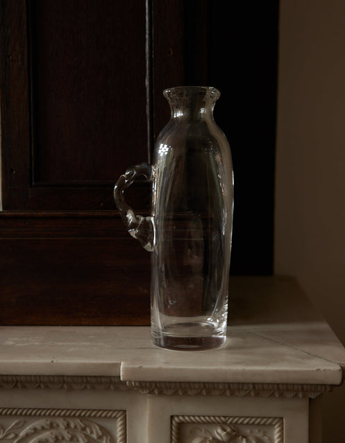 Large water carafe | Glass: A clear glass carafe with an ornamental handle, set on a marble shelf, showcasing Szkło Studio's unique, hand-blown craftsmanship.