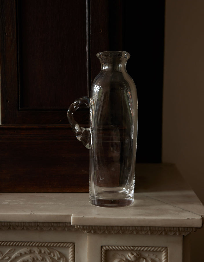 Large water carafe | Glass: A clear glass carafe with an ornamental handle, set on a marble shelf, showcasing Szkło Studio's unique, hand-blown craftsmanship.