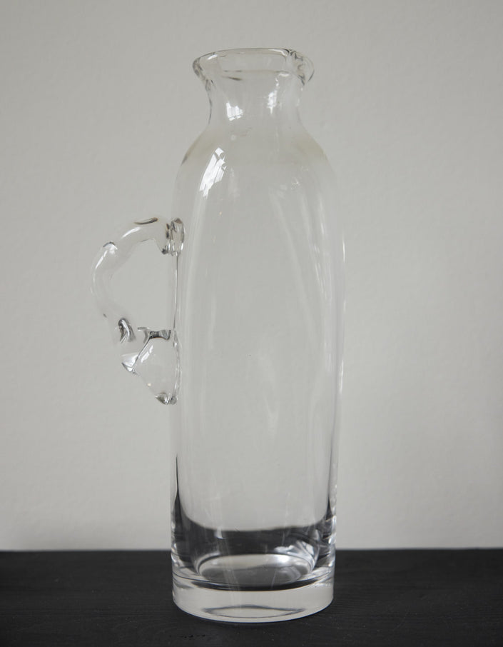Large water carafe | Glass: A clear glass carafe with an ornamental handle, set on a marble shelf, showcasing Szkło Studio's unique, hand-blown craftsmanship.