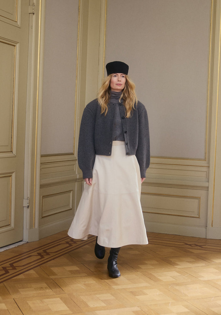 Woman in a charcoal turtleneck under a matching cardigan, showcasing the Double-layer wool top | mid grey melange, paired with a cream skirt and black boots.