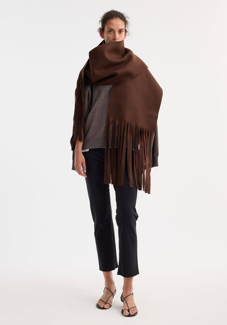 Model wears an oversized Wool scarf | pure chocolate, draped over a grey sweater, paired with black trousers and sandals, showcasing relaxed elegance.