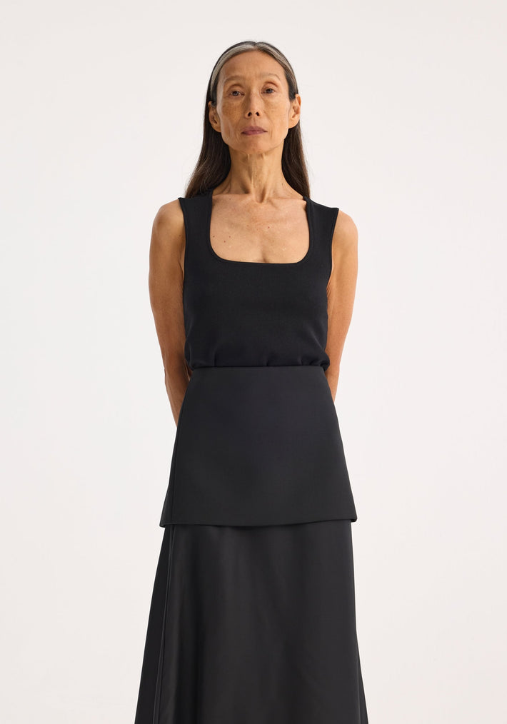 Woman wearing Bustier shaped knitted top with square neckline, fitted design, arms behind back, long skirt; minimalist fashion portrait.