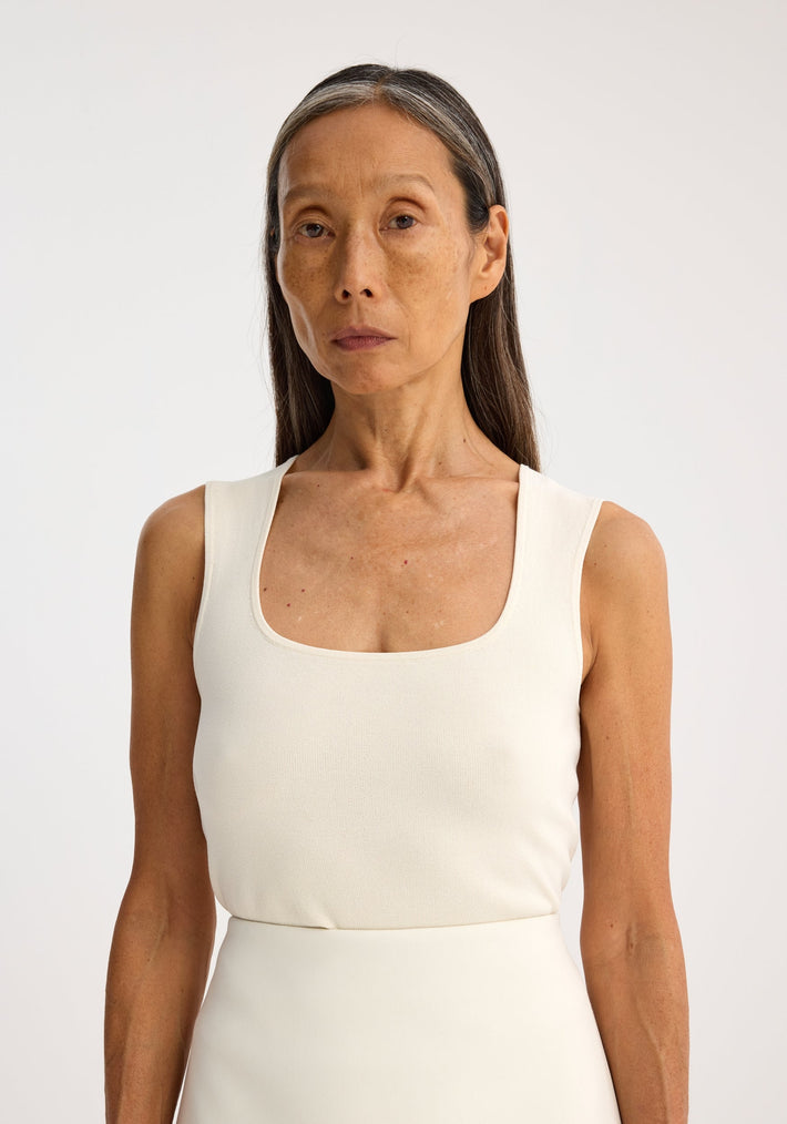 Woman wearing Bustier shaped knitted top with square neckline, off-white color, posed against light background. Sleeveless design highlights fitted, versatile style.