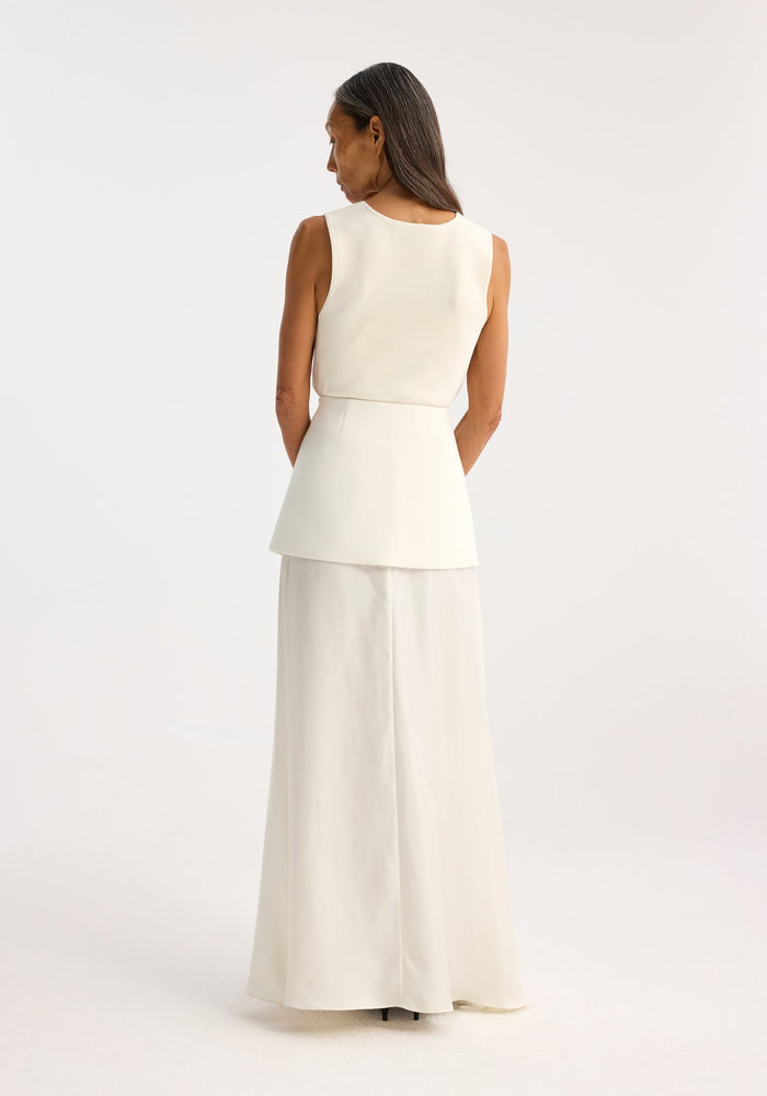 Woman wearing an off-white bustier shaped knitted top with a fitted design, paired with a matching floor-length skirt, viewed from behind.