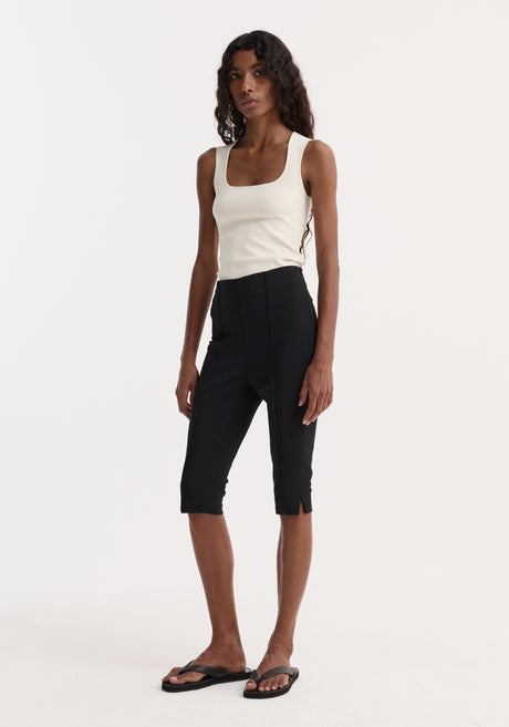 Model wearing Bustier shaped knitted top, off-white with square neckline, paired with high-waisted black capri trousers and black flip-flop sandals against a plain background.