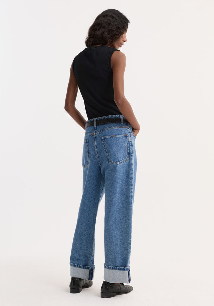 Model in dense rib tank top, black, tucked into high-waisted jeans with wide, cuffed legs. The tank is slim-fit, organic cotton, highlighting versatility.