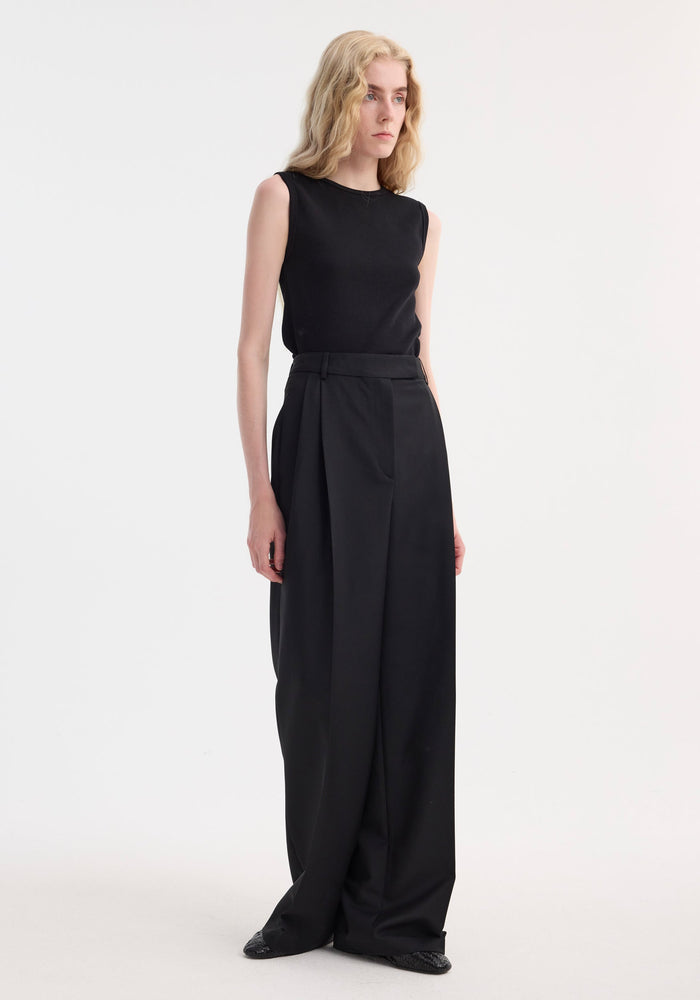Model in Dense Rib Tank Top | black, featuring a fitted sleeveless design and fine-rib texture, paired with high-waisted, wide-leg trousers for a minimalist look.