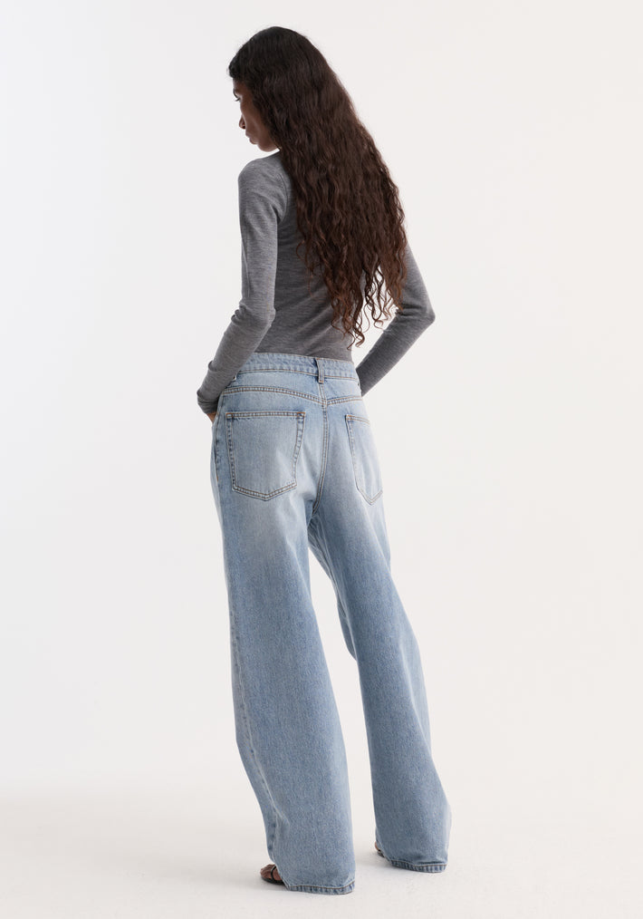 Person with wavy dark hair wearing the Fine merino turtleneck in mid grey melange, tucked into high-waisted, wide-leg jeans, standing back to camera.