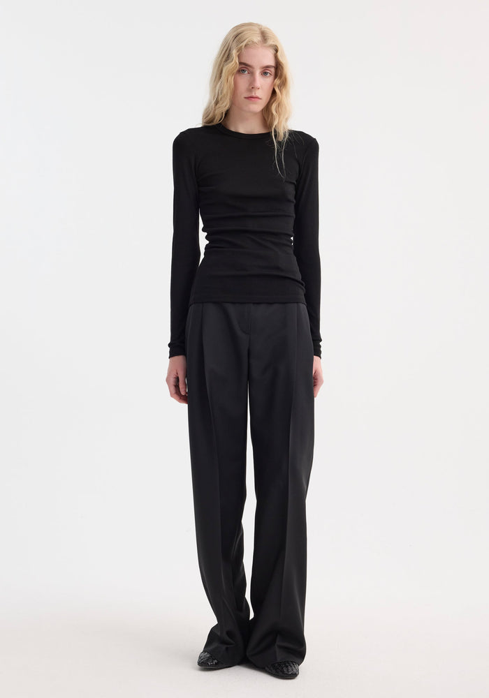 Model wears Fine merino long sleeve in black, a crew neck, form-fitting top crafted from 100% merino wool, tucked into high-waisted, wide-leg trousers.