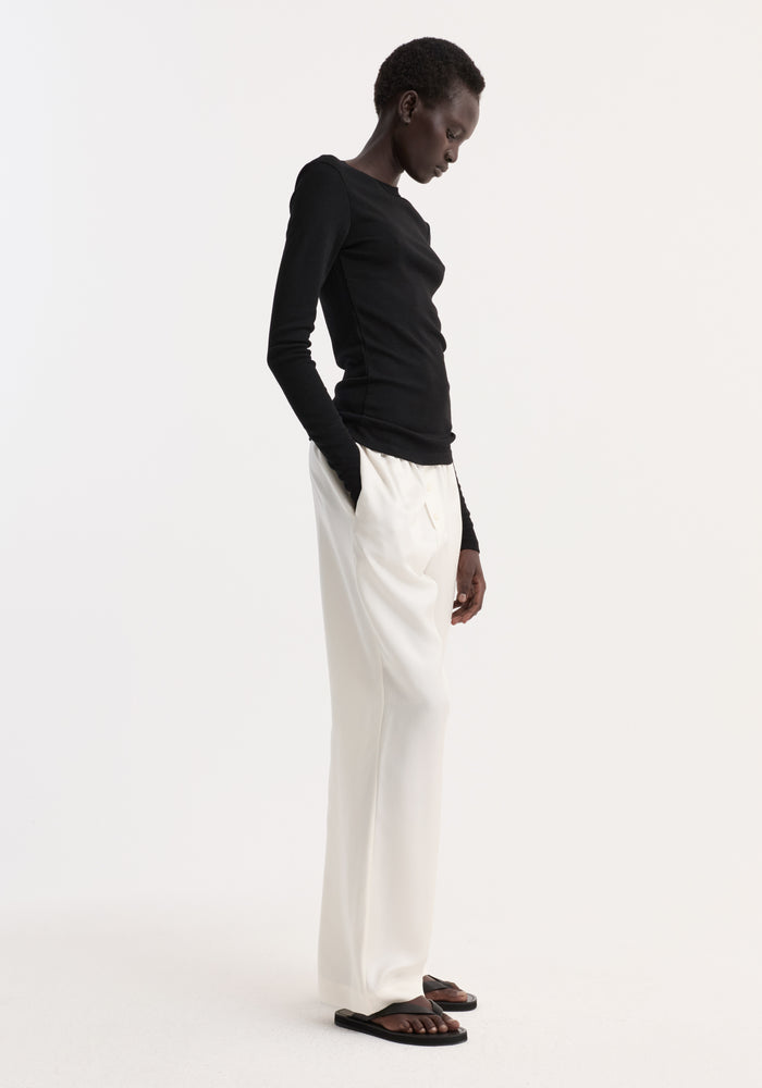 Fine merino long sleeve in black, worn fitted and tucked into high-waisted trousers, styled with casual sandals for a minimalist, modern look.