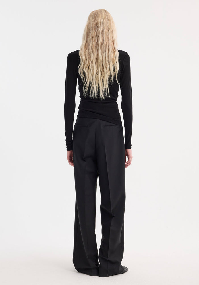 Model with back turned showcases Fine merino long sleeve | black, featuring a fitted silhouette and crew neck, paired with wide-leg trousers.