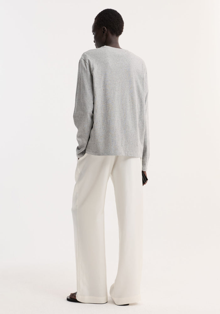 Slub melange cotton long sleeve in light grey, oversized fit, worn by a person with wide-leg trousers, holding a black wallet, exuding a minimal, relaxed style.