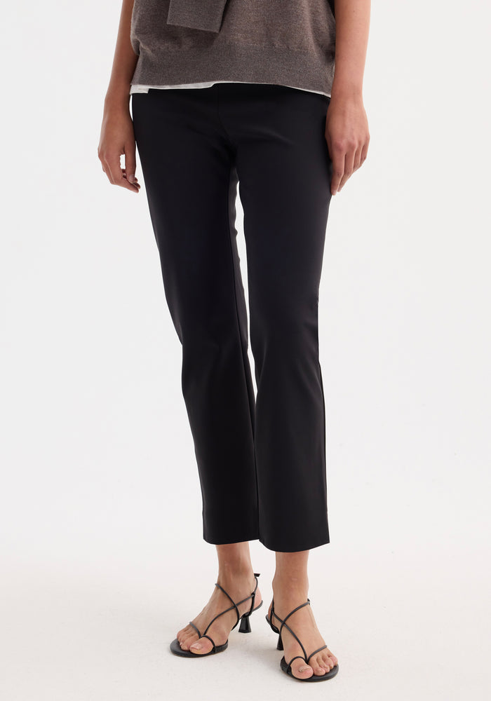 Cigarette scuba trousers in black, showcasing a tailored ankle-length silhouette, modeled with strappy heeled sandals against a plain white background.