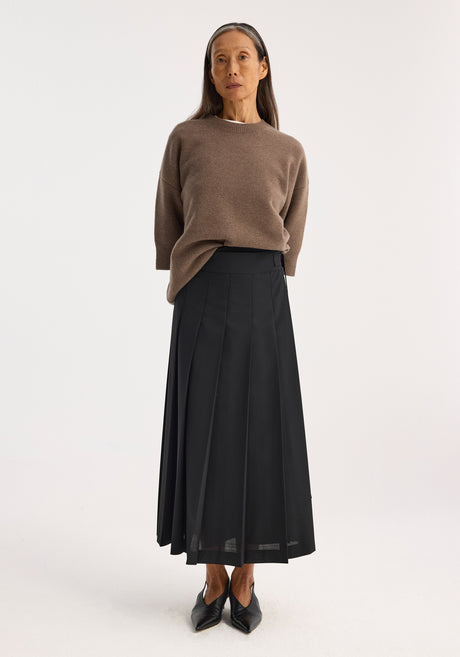 Plissé wrap skirt in black featuring a mid-length pleated design, adjustable placket strap closure, and belt detail for a refined silhouette.