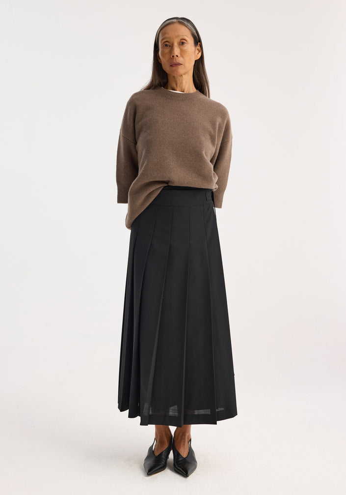 Plissé wrap skirt in black featuring a mid-length pleated design, adjustable placket strap closure, and belt detail for a refined silhouette.