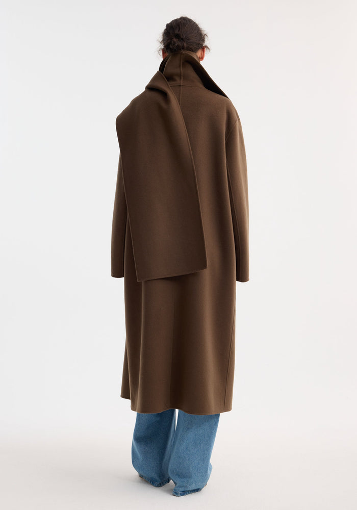 Back view of model wearing Signature double-faced scarf coat with double-layered collar, over light blue wide-leg jeans, highlighting the coat's long length and sophisticated design.