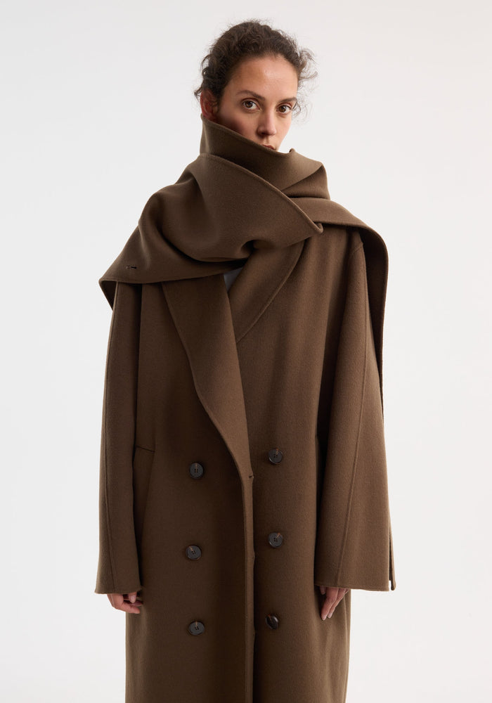 Signature double-faced scarf coat modeled with oversized scarf collar, double-breasted design, six buttons, side pockets, and long length, showcasing luxurious 100% wool craftsmanship.