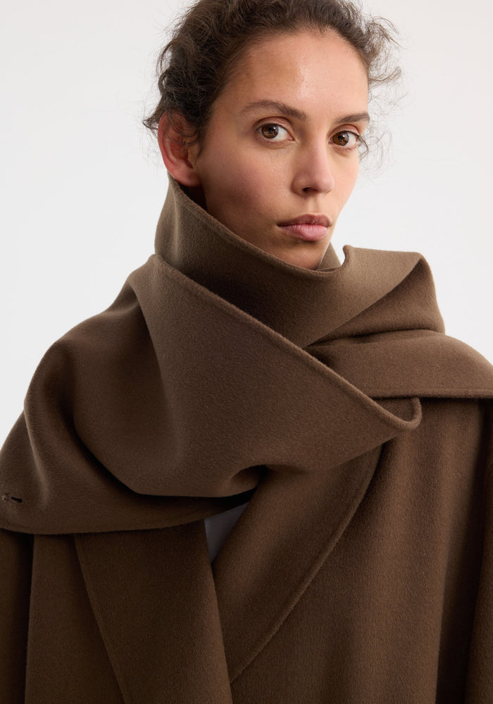 Close-up of a person wearing the Signature double-faced scarf coat in taupe, highlighting its thick wool material and distinctive double-layered scarf collar.