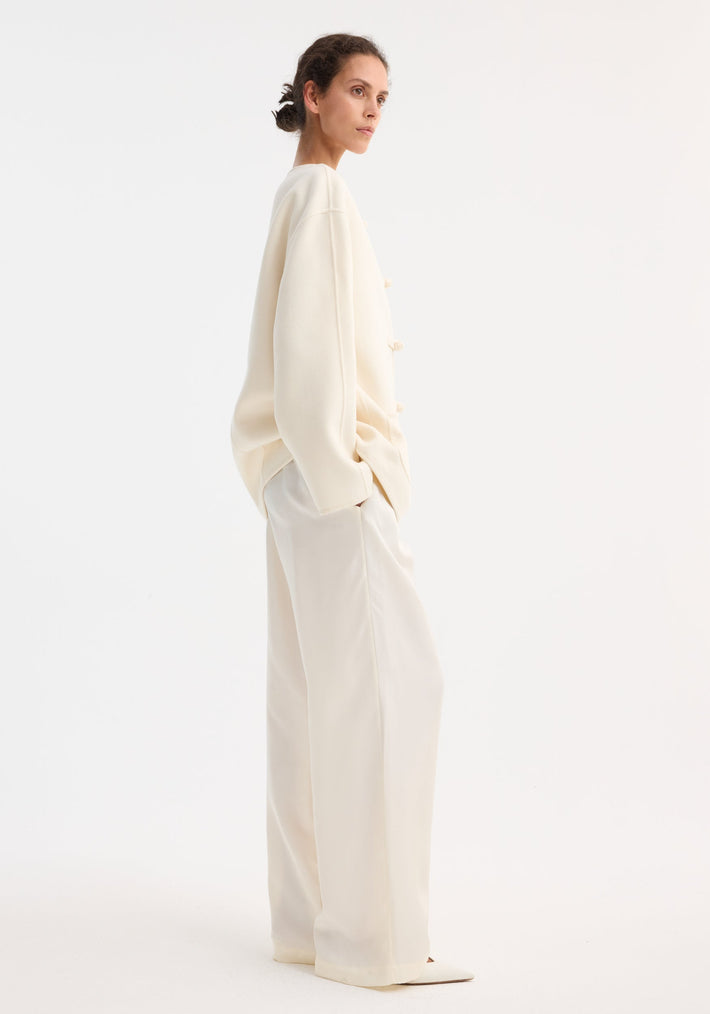 Model in profile wearing the Mandarin double-faced wool jacket with pankou closure, paired with wide-leg trousers and pointed-toe shoes, embodying a minimalist, monochromatic style.