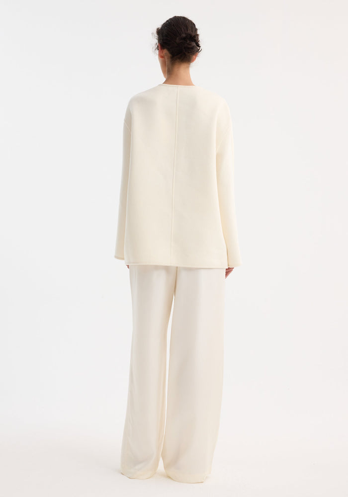 Back view of a person wearing an oversized, off-white Mandarin double-faced wool jacket with a center seam and relaxed fit, paired with matching wide-leg trousers.