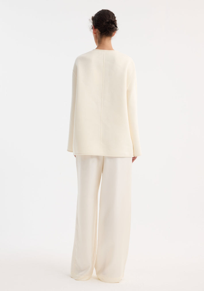 Back view of a person wearing an oversized, off-white Mandarin double-faced wool jacket with a center seam and relaxed fit, paired with matching wide-leg trousers.