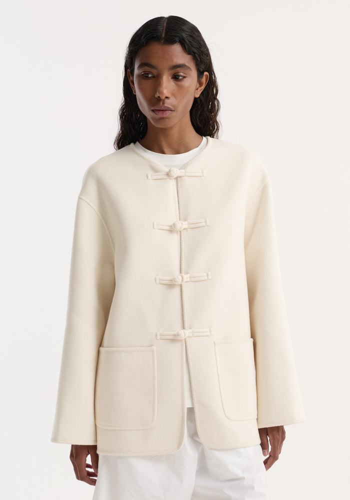Model wearing a double-faced wool pankou jacket in off-white, featuring embroidered edges, patch pockets, and traditional pankou knot closures for an elegant, minimalist look.