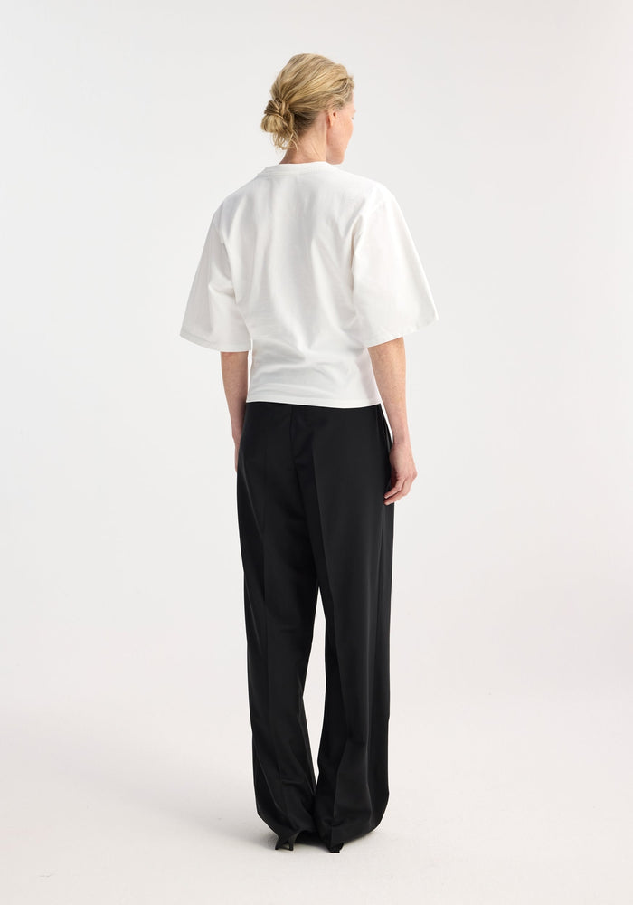 Back view of person wearing Fitted logo t-shirt in optic white, showcasing crew neck, tapered sleeves with logo, paired with high-waisted black trousers.