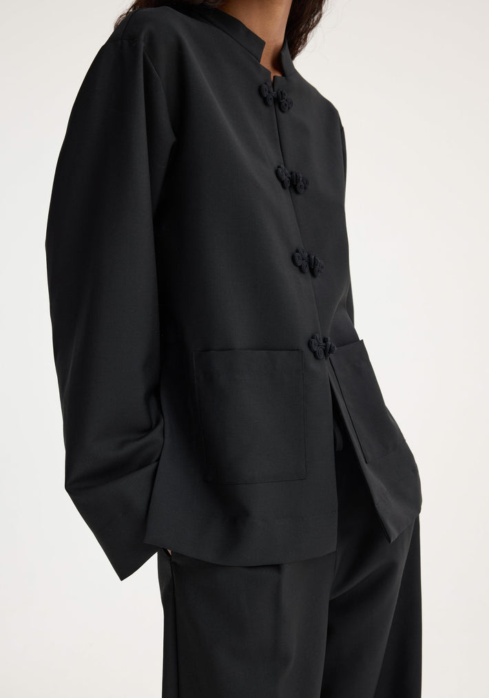 Mandarin jacket | black with traditional frog knot buttons, patch pockets, and mandarin collar, worn with matching trousers. Virgin wool and mohair blend.