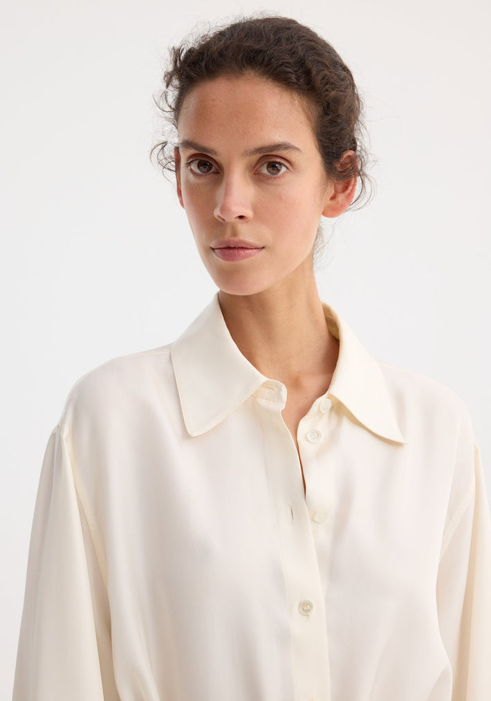 Woman wearing Deconstructed silk shirt | cream with a pointed collar, showcasing its open back and versatile tie detail, looking directly at the camera.