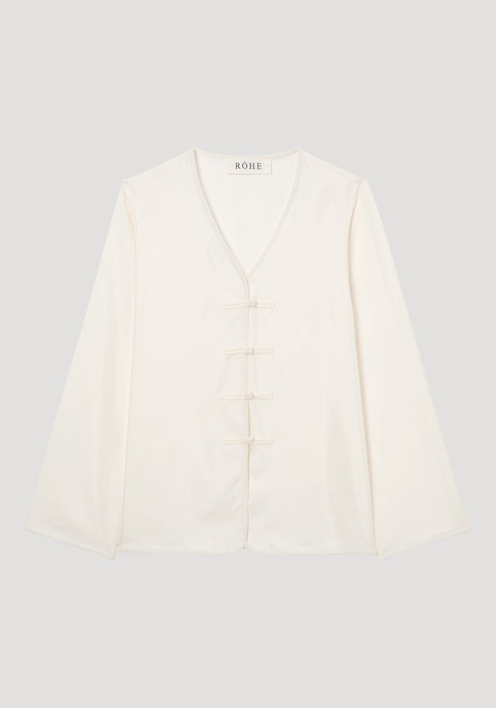 Mandarin silk top in ivory cream with V-neck, flared sleeves, pankou closures, and embroidered edges, laid flat on neutral background, showcasing a relaxed fit.