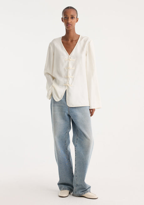 Model in Mandarin silk top with V-neck, pankou closures, and embroidered edges, paired with straight-leg jeans and slip-on shoes.