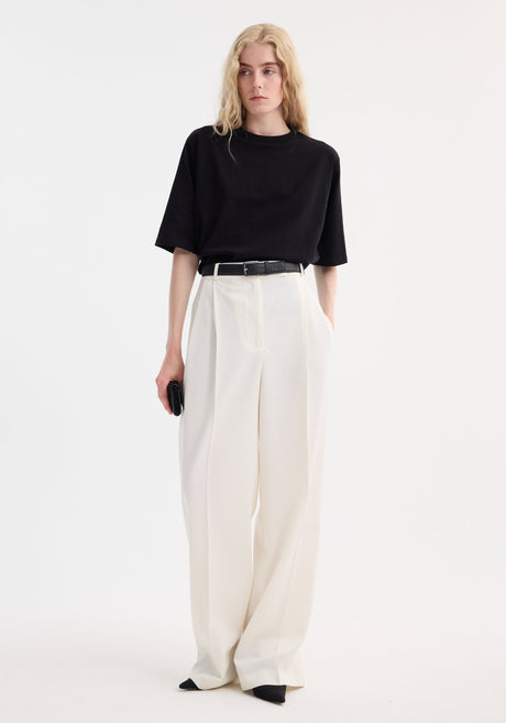 Slim person wearing an Oversized cotton t-shirt in black, tucked into high-waisted trousers, holding a black accessory, showcasing the shirt’s relaxed fit and crew neck design.