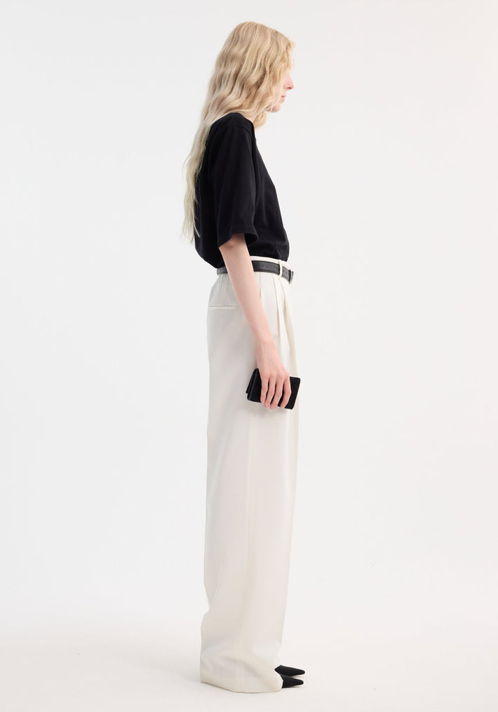 Side profile of a tall person wearing an Oversized cotton t-shirt | black, paired with wide-leg trousers, holding a small black wallet.