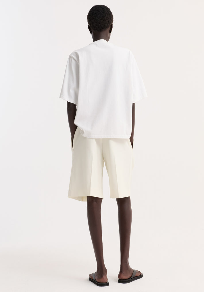 Model in Oversized cotton t-shirt | optic white, showcasing its relaxed fit and drop shoulder, paired with tailored shorts and slide sandals for a minimalist look.