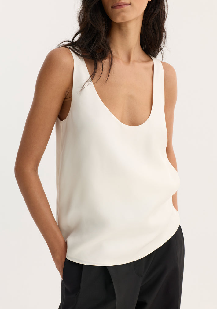 Person wearing a cream scoop-neck silk top with a loose fit, showcasing its minimalist design and signature flowing silk quality.