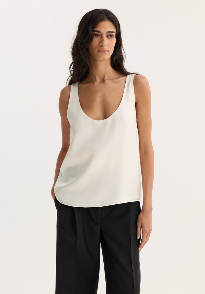 Woman wearing scoop-neck silk top, cream, with a loose fit, paired with black trousers. Ideal for minimalist capsule wardrobes, showcasing pure silk elegance.