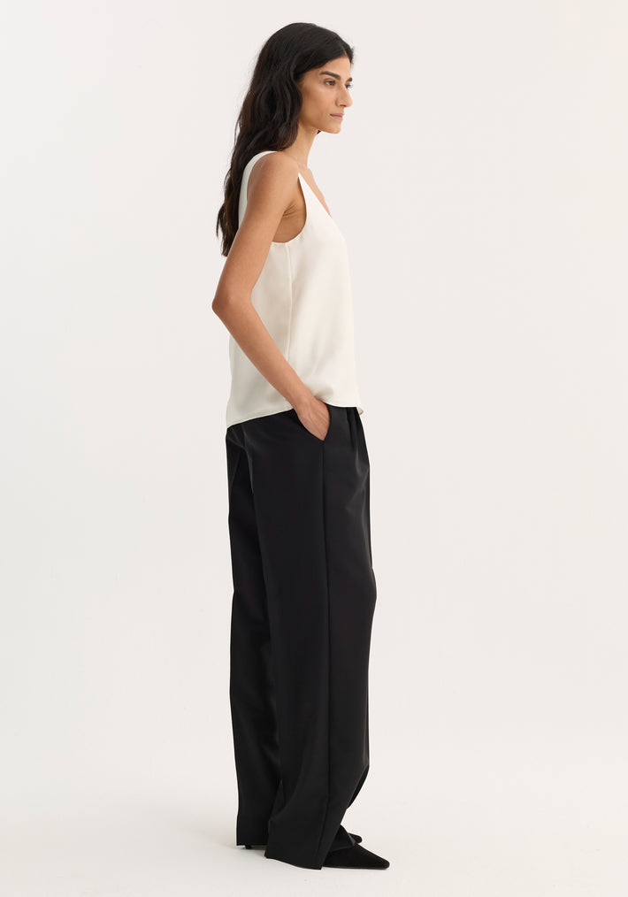 Model wearing a scoop-neck silk top in cream, featuring a loose fit and minimalist design, paired with high-waisted black trousers and pointed-toe shoes.