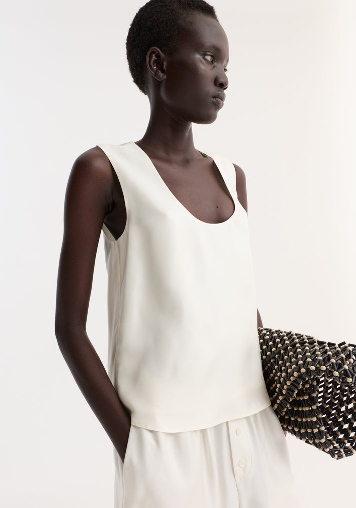 Model wearing Scoop-neck silk top | cream, featuring a loose fit and wide scoop neckline, paired with matching bottoms and holding a woven black clutch.