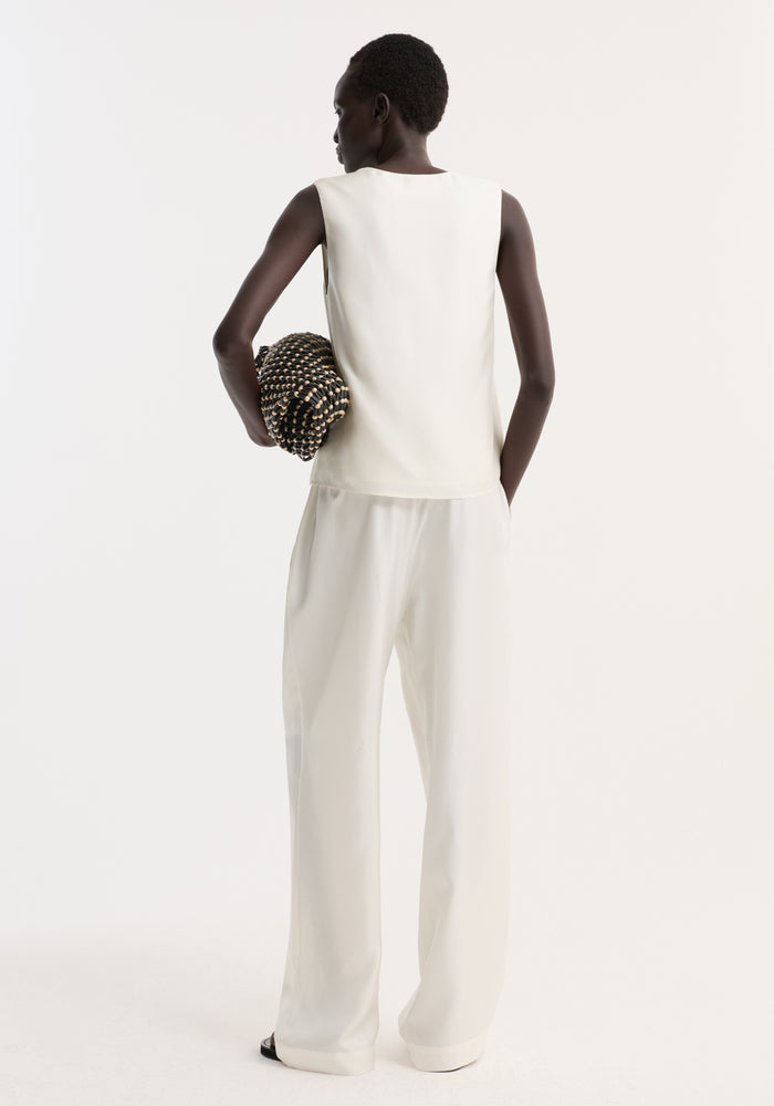 Model wearing scoop-neck silk top in loose fit, showcasing its soft, flowing quality. She holds a black and wooden beaded clutch, embodying minimalist style.