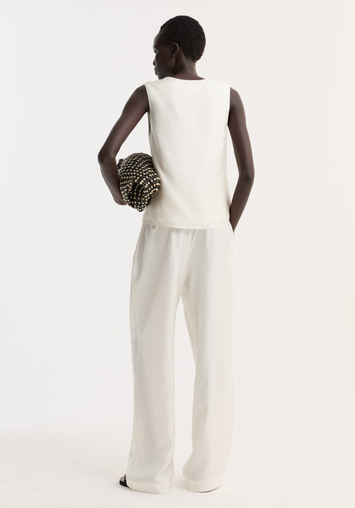Model wearing scoop-neck silk top in loose fit, showcasing its soft, flowing quality. She holds a black and wooden beaded clutch, embodying minimalist style.