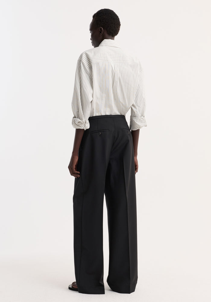 Model wearing Relaxed drawstring trousers in black, featuring wide-leg design, drawstring waistband, and front pleats, paired with an off-white pinstripe shirt.