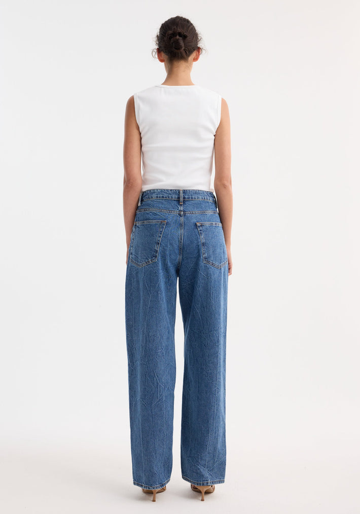 Rear view of a person in Signature baggy fit denim, mid denim blue, with wide-leg, low-waist design, paired with a sleeveless ribbed tank top.