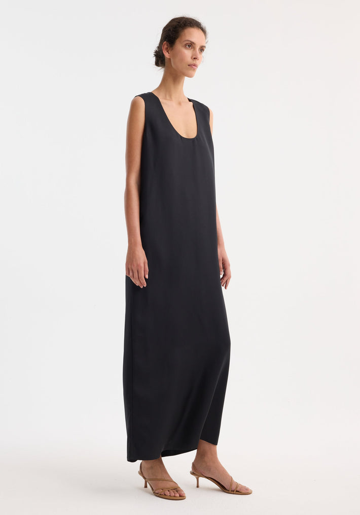 Woman modeling Scoop-neck silk dress | black, floor-length, sleeveless, deep scooped neckline, relaxed silhouette, paired with tan strappy low-heel sandals.