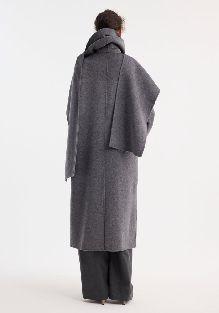 Signature double-faced scarf coat in mid grey melange, featuring a double-layered scarf collar, worn over wide-leg trousers and neutral pointed-toe heels, seen from behind.