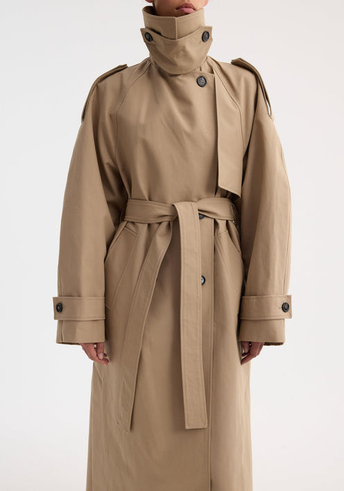 Model in Oversized classic trench | clay, featuring double-breasted design, epaulettes, belted waist, and side pockets, over black cropped trousers and strappy sandals.
