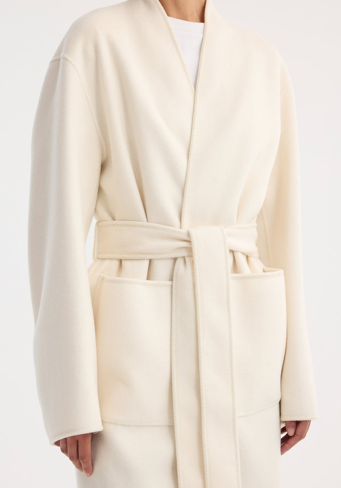 Double-faced kimono style coat in off white, featuring a wrap design, self-tie belt, long sleeves, and patch pockets, showcasing a minimalist, elegant silhouette.